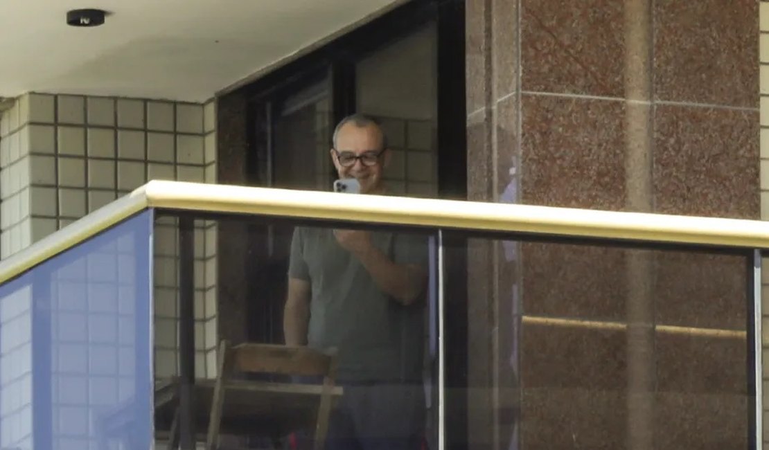Ainda sem poder sair do prédio, Cabral fala ao celular e ri na sacada do apartamento