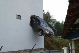 Motorista acelera em garagem e carro fica pendurado fora do prédio